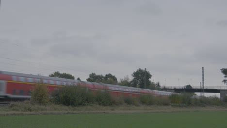 Red-passenger-train-in-motion-on-a-cloudy-day,-blurred-by-speed,-with-greenery-in-the-foreground