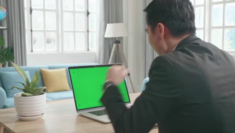 asian businessman wearing business suit with green screen computer being happy successful in work while working at home.
