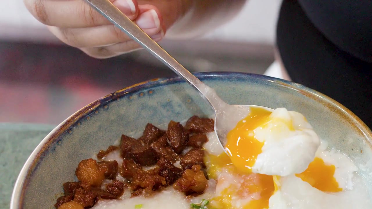 Person Scooping Poached Egg from Bowl of Congee