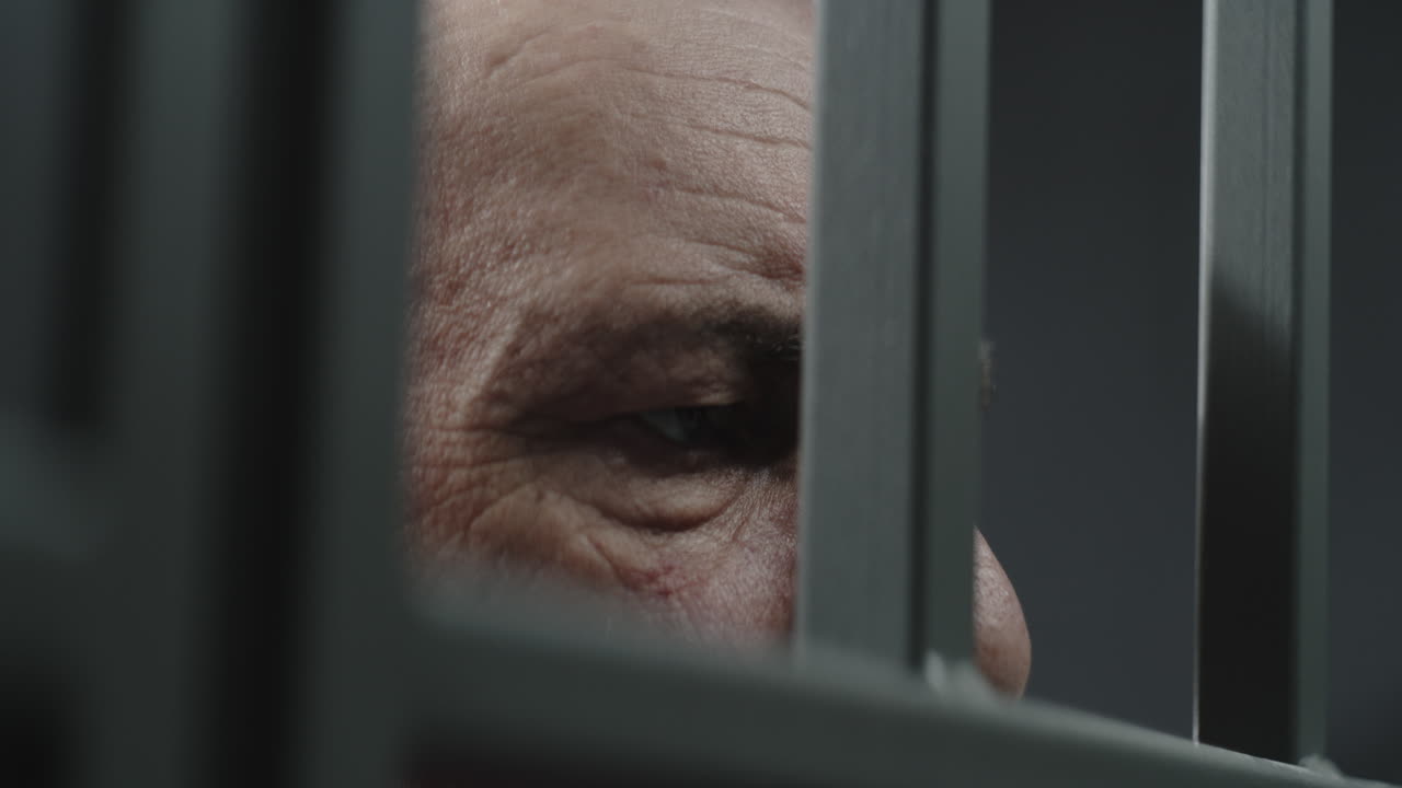 primer plano de un prisionero en uniforme naranja sosteniendo barras de metal en una celda de la prisión (imágenes de stock)