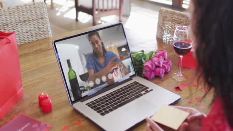 Happy-african-american-man-with-wine-making-valentine's-day-video-call-on-laptop