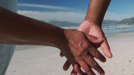 Midsection-of-senior-african-american-couple-walking-and-holding-hands-at-the-beach