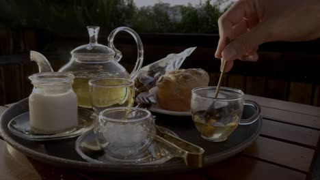 womans hand mixing glass of herbal tea sitting on a breakfast tray