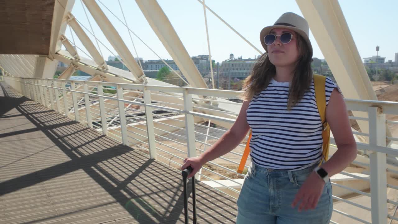 A woman is walking with a green suitcase on a bridge.