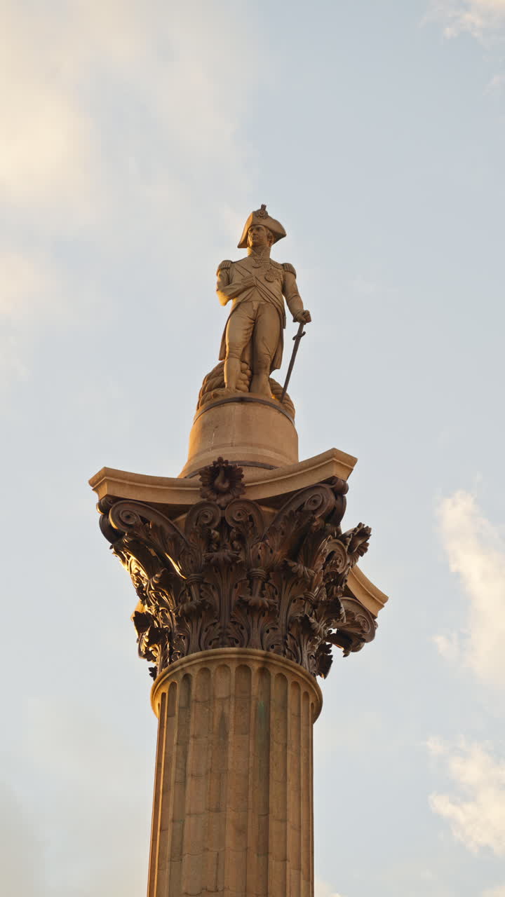 Close-up view of an the towering column of Nelson's Column in Trafalgar Square, with blue skies and scattered clouds in the background. Vertical, London