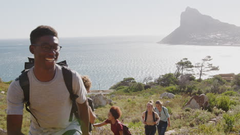 group of young friends hiking up cliffs on coastal path through countryside together