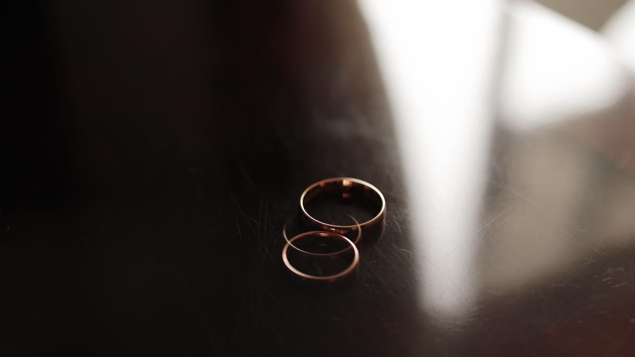 Two simple gold wedding rings on a dark reflective wooden surface in soft natural light