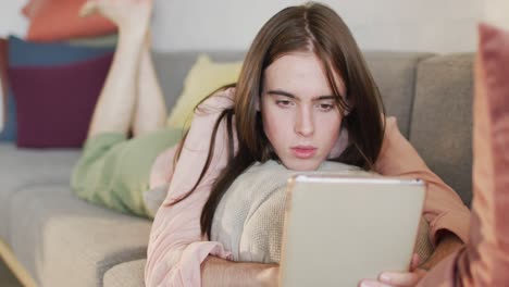 mujer transgénero caucásica no binaria acostada en el sofá, usando una tableta