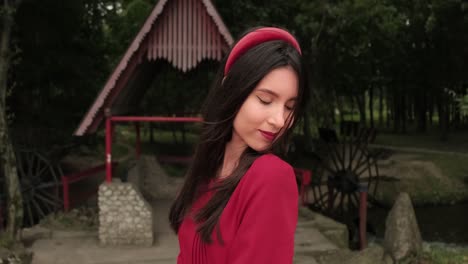 woman in red dress posing by a traditional water wheel and bridge