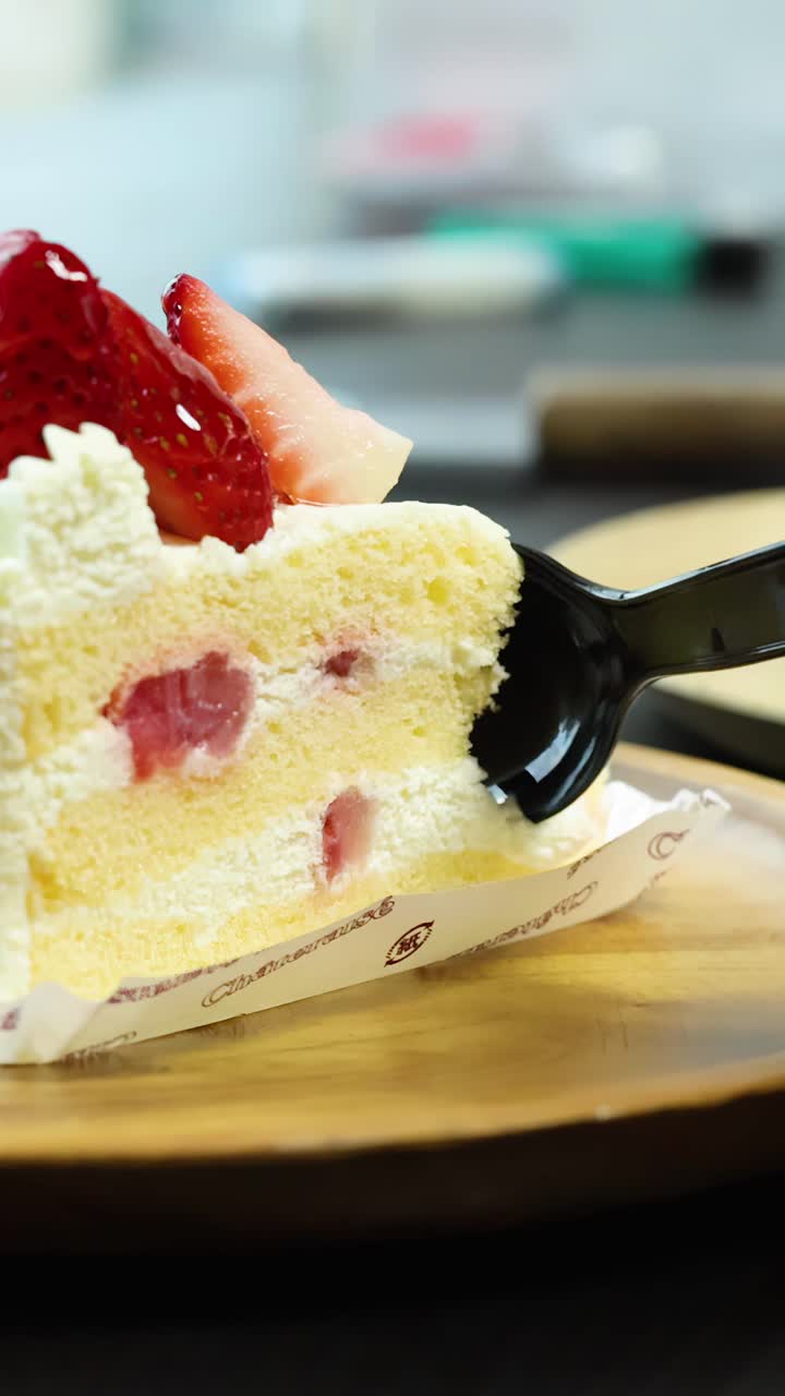 Black spoon slices through strawberry shortcake on wooden plate, soft lighting, shallow depth of field
