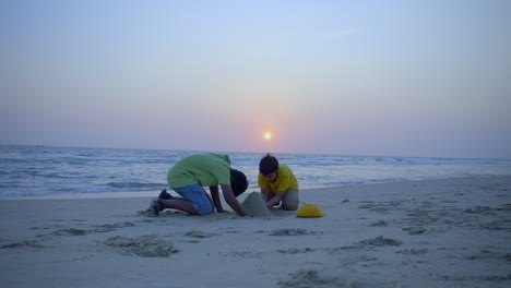 boys building a sandcastle at the beach in sunset