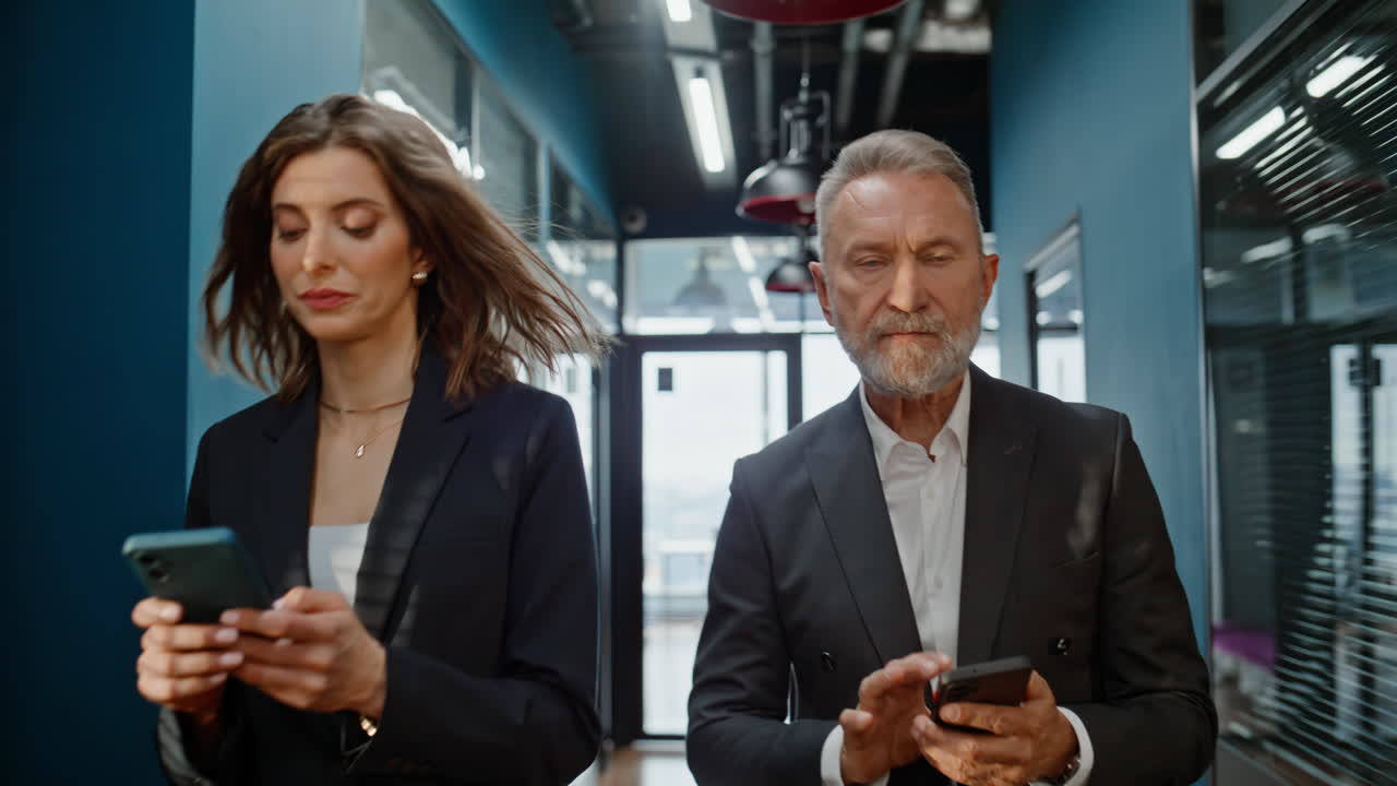 Successful businesspeople walking hallway looking cellphones closeup. Partners