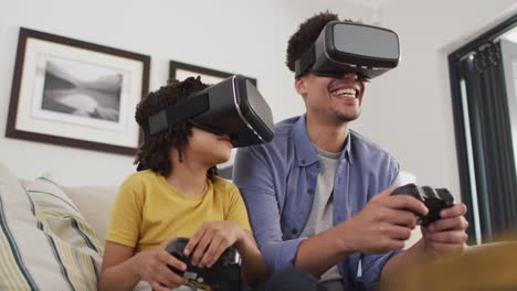 hombre biracial feliz y su hijo jugando videojuegos usando auriculares vr