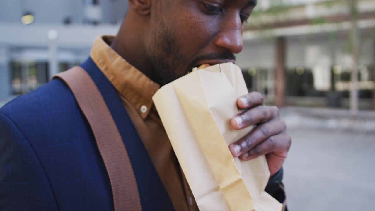 hombre de negocios afroamericano comiendo sándwich en la calle de la ciudad