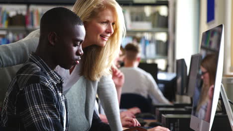 Lehrer-Mit-Männlichem-Studenten,-Der-In-Der-Universitätsbibliothek-Am-Computer-Arbeitet