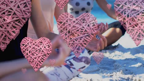 Animation-of-pink-hearts-over-low-section-of-women-meditating-on-sunny-beach