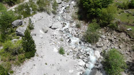 Drohnenansicht-In-Albanien-In-Den-Alpen,-Die-über-Einen-Kristallklaren-Fluss-Mit-Felsigem-Boden-Und-Grünem-Wald-An-Den-Seiten-Im-Theth-Fliegt