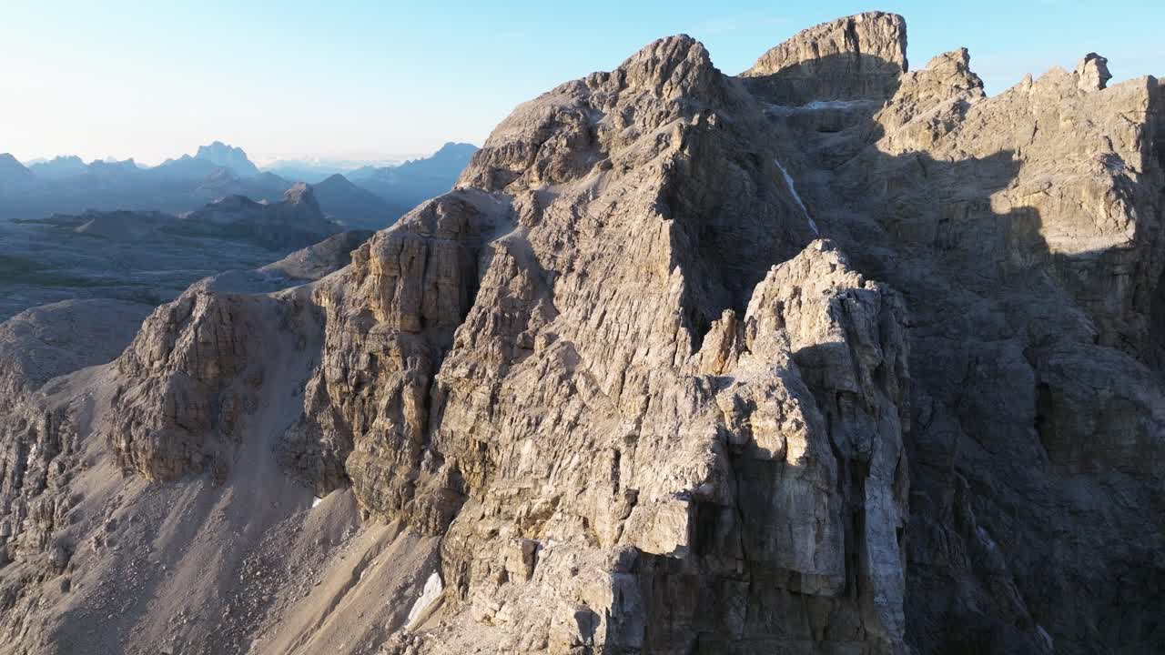 A magnificent view of the Dolomites, highlighting jagged rock formations bathed in soft sunlight, with distant peaks casting silhouettes against the clear sky