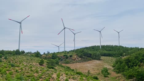 renewable energy topic – wind power plant propellers fast turning among setting of shrubland hills and overcast sky