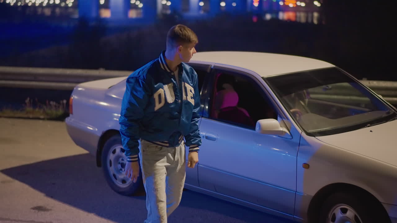Joven caucásico saliendo de un sedán blanco bajo un horizonte de neón, alejándose hacia las luces de un puente, con chaqueta universitaria azul y actitud introspectiva, ambiente cinematográfico nocturno y silenciosa determinación
