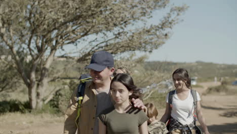 Caucasian-family-with-backpacks-walking-along-dirt-road-and-talking-together