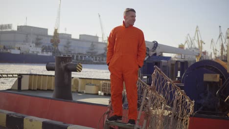 young worker in the uniform posing on the bridge of a ship, about to moor off in a city harbor