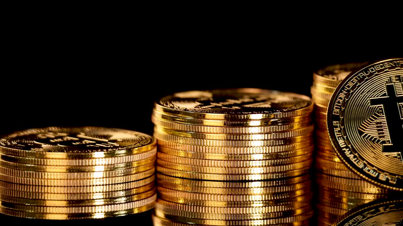 Gold digital coin rotates upright on stacked coins, dramatic lighting, black background, close-up view