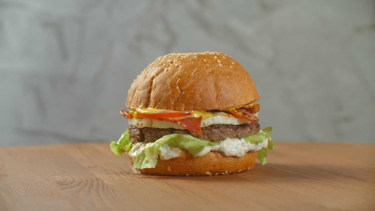 la hamburguesa gira en una tabla de madera. una hamburguesa con un queso de ensalada y tomates gira contra una pared gris