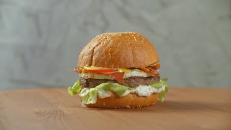 The-hamburger-spins-on-a-wooden-Board.-A-Burger-with-a-cutlet-salad-cheese-and-tomatoes-revolves-against-a-gray-wall