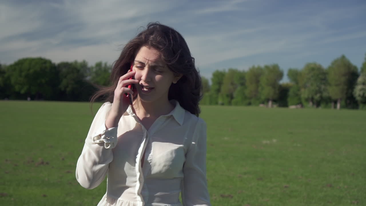 공원을 산책하고 전화 통화를 하는 동안 기분이 좋은 젊은 아름다운 이탈리아 소녀의 스테디캠 샷