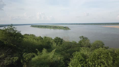 drone fly out past pagoda on the shores of mekong revealing a lush island in the middle of the river