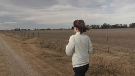 slow motion, wide view of a young adult female walking with her pet dog in a rural road