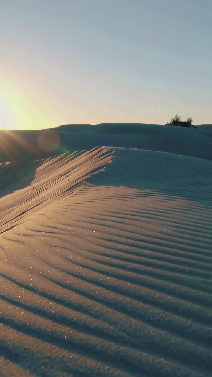 Video verticale: Sole basso che si sposta, telecamera in movimento e inclinazione tra le dune, rivelando creste ondulate.