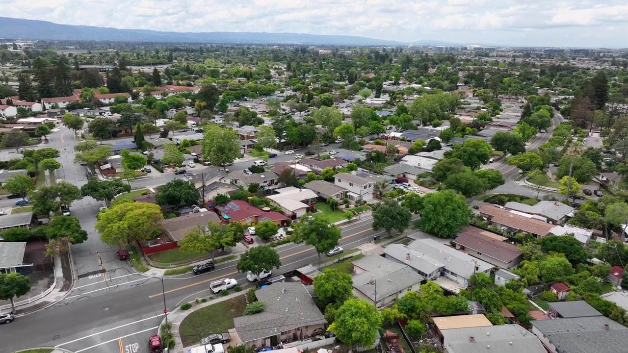 Quartiere residenziale denso con case unifamiliari e strade alberate, l'espansione pianeggiante della Silicon Valley che si estende verso la catena montuosa sotto un cielo parzialmente nuvoloso. California, USA. Ripresa aerea.
