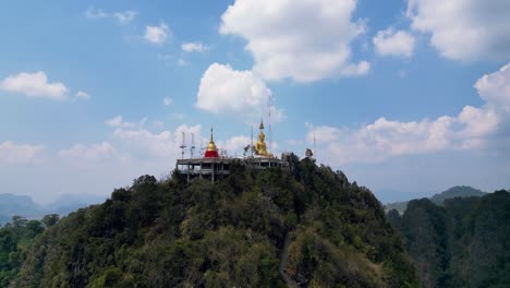 aerial view of wat tham suea with golden buddha atop lush mountain under blue sky in krabi, thailand