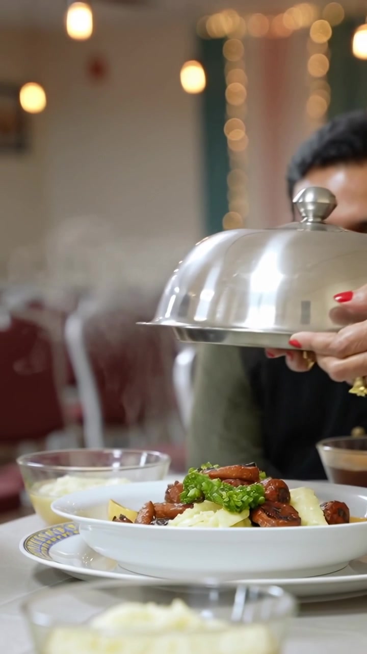 Vertical video: Lifting cloche, woman's hand showing hot mash with sausage for family at banquet