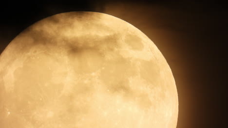 dark clouds move past a bright, orange, full moon