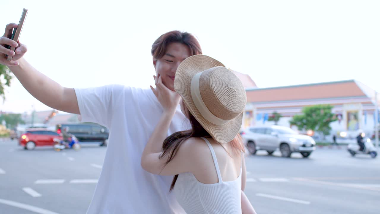 คู่รักหนุ่มสาวมีความสุขกับการถ่ายเซลฟี่ด้วยสมาร์ทโฟนขณะเที่ยวชมถนนในเมืองกรุงเทพฯ ที่มีแสงแดดสดใส