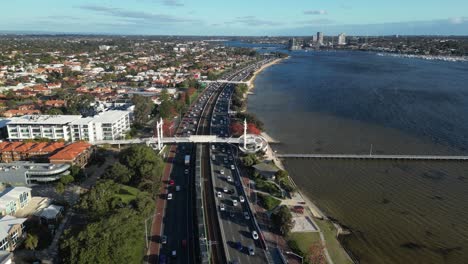 Vista-Aérea-De-La-Concurrida-Carretera-Costera-Con-Tráfico-En-El-Río-Swan-En-La-Ciudad-De-Perth-Durante-La-Puesta-De-Sol,-Australia---Inclinada-Hacia-Arriba