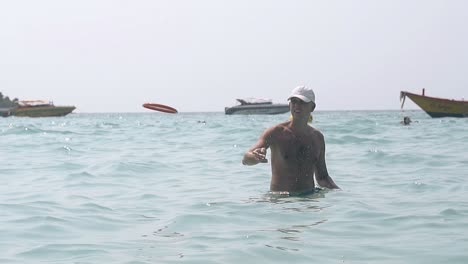 young man throws frisbee in sea water on day slow motion