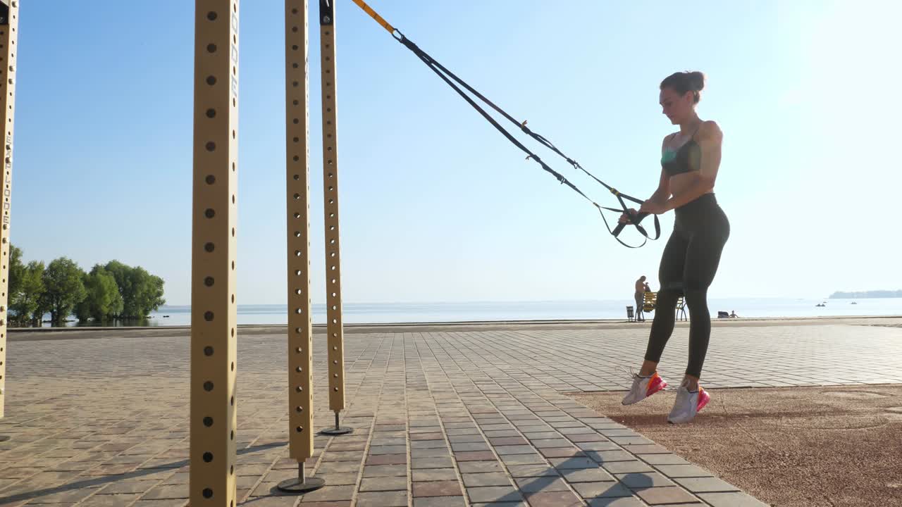 entrenamiento al aire libre. correas de suspensión. entrenamiento con correas. mujer joven atlética está haciendo ejercicios de resistencia de todo el cuerpo usando cuerdas en bucle trx, en la playa durante la puesta o el amanecer. entrenamiento de fitness al aire abierto. concepto de estilo de vida saludable. deporte matutino