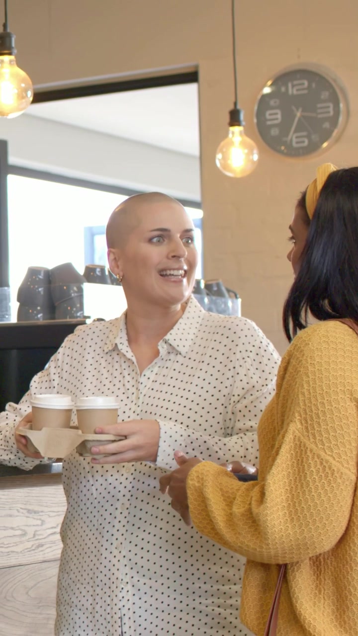 Video verticale: Donna rasata con top a pois che offre un vassoio a una donna in giallo al caffè quando gli ordini sono pronti.