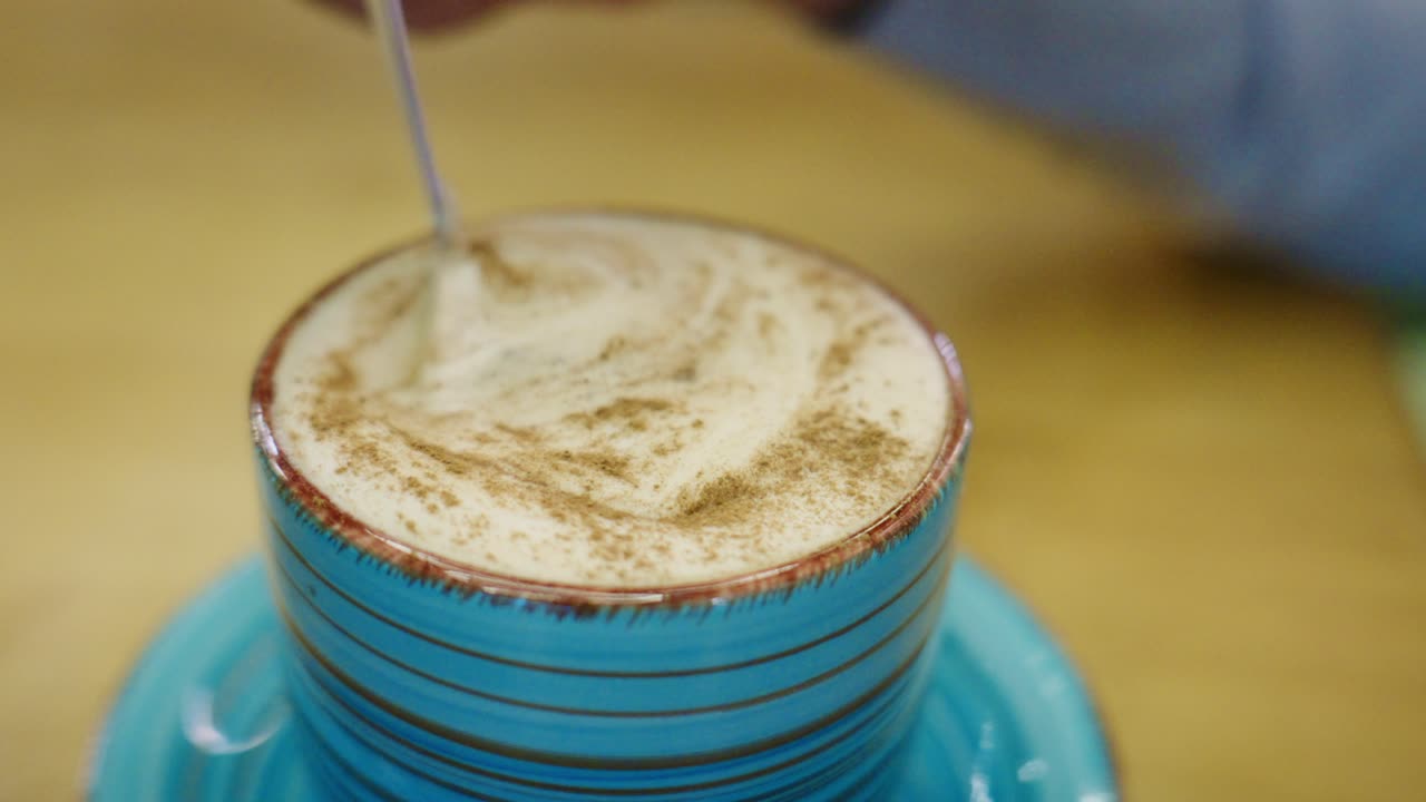 Cucchiaino che mescola caffè schiumoso con cannella in una tazza blu