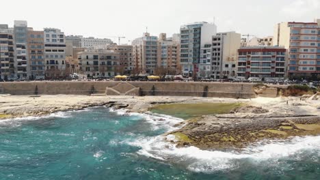 Sliema-city-seafront-with-Promenade-leading-to-rocky-beach-in-Malta---Descending-aerial-shot