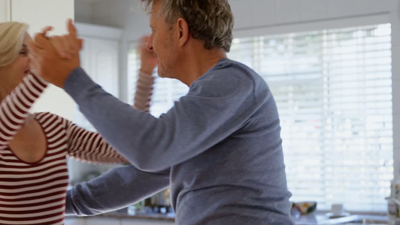 Side view of mature caucasian couple dancing together in kitchen at home 4k