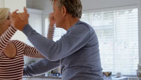 Side-view-of-mature-caucasian-couple-dancing-together-in-kitchen-at-home-4k