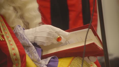 mano de san nicolás con guante blanco y anillo de rubí hojeando a través del santo libro rojo