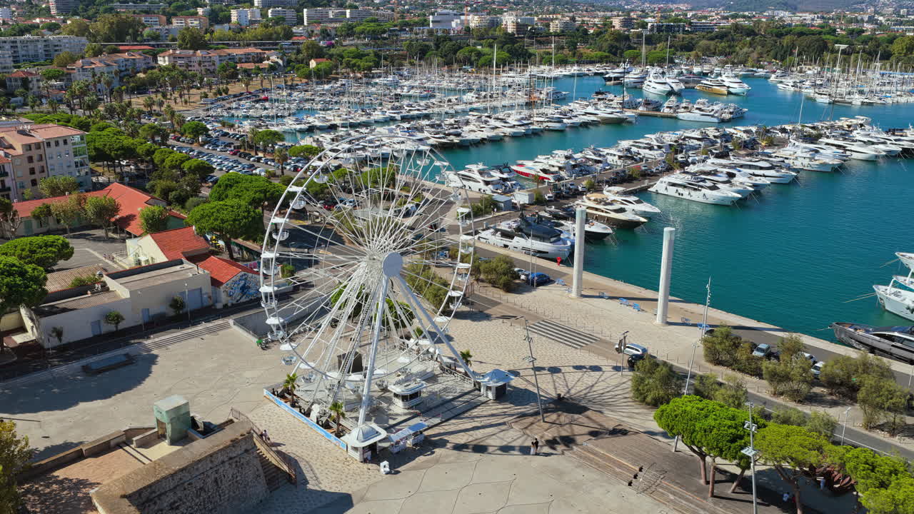 Aerial drone view of the Ferris wheel in Antibes near the marina, with hundreds of yachts docked in the port and the mountains in the background