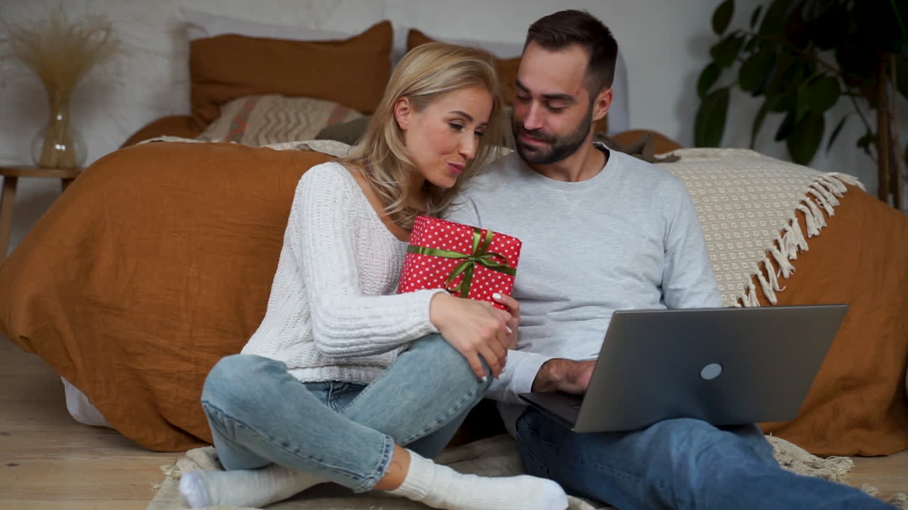 encantadora pareja haciendo videollamadas con su familia y mostrando un regalo de navidad 1