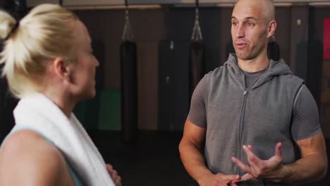 Caucasian-male-trainer-talking-to-fit-caucasian-woman-at-the-gym